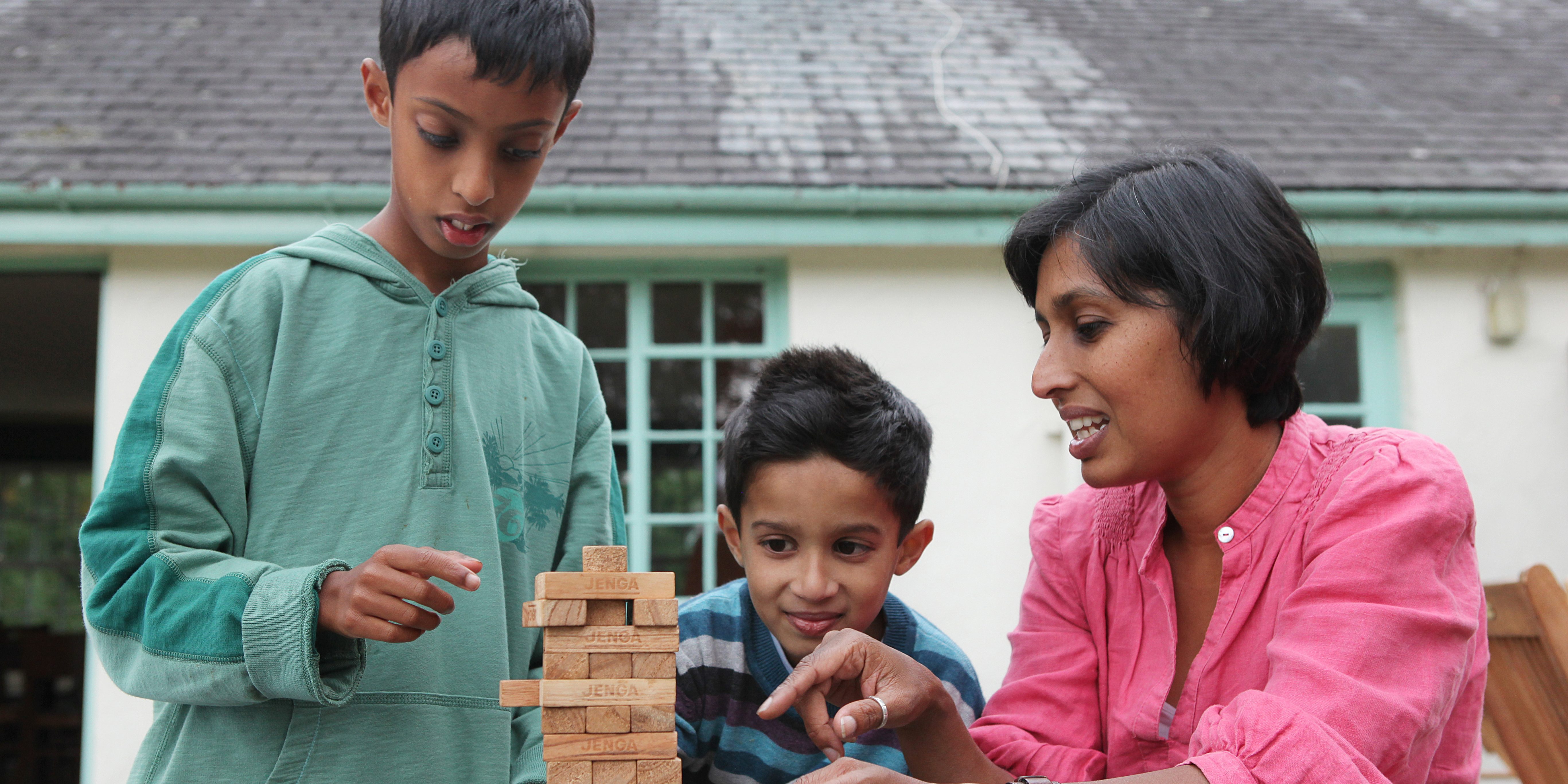 Asian boy with Autism in the garden playing a game of Jenga with his mother and his younger brother